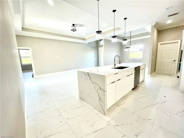 Kitchen featuring crown molding, white cabinetry, light marble finish floors, light stone countertops, and pendant lighting