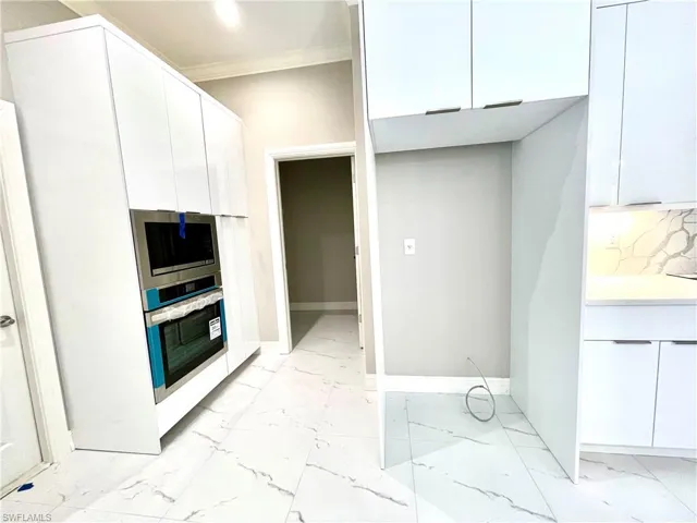 Kitchen with crown molding, stainless steel appliances, white cabinetry, light marble finish floors, and decorative backsplash