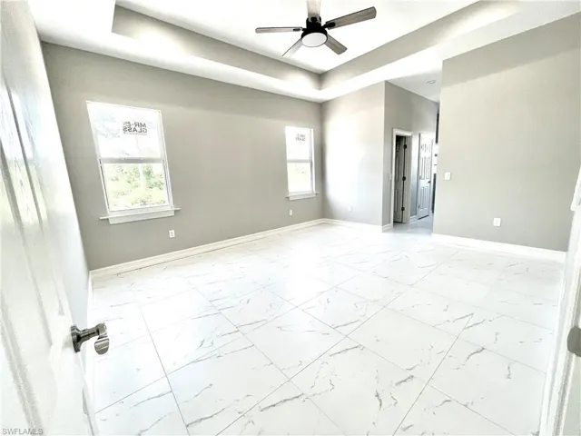 Unfurnished room featuring a tray ceiling, light marble finish flooring, and ceiling fan