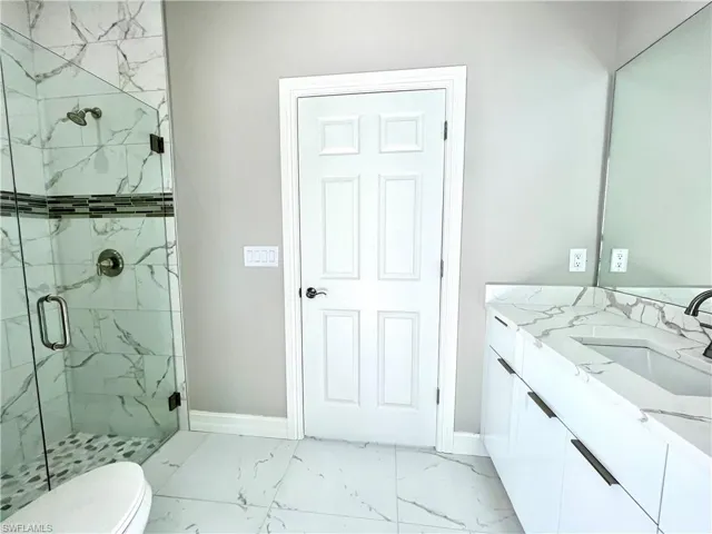 Bathroom with light marble finish floors, a marble finish shower, and vanity