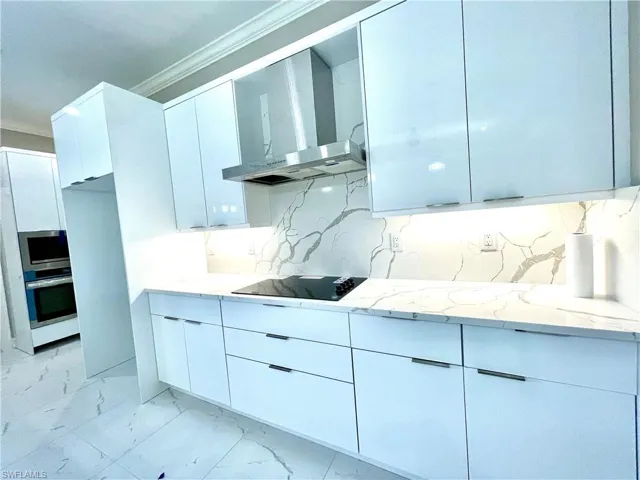 Kitchen featuring modern cabinets, wall chimney range hood, ornamental molding, light stone countertops, and light marble finish floors
