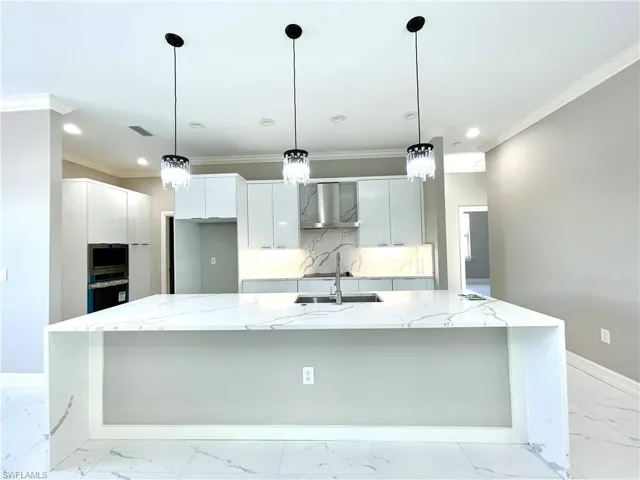 Kitchen featuring light stone counters, crown molding, pendant lighting, wall chimney exhaust hood, and a large island