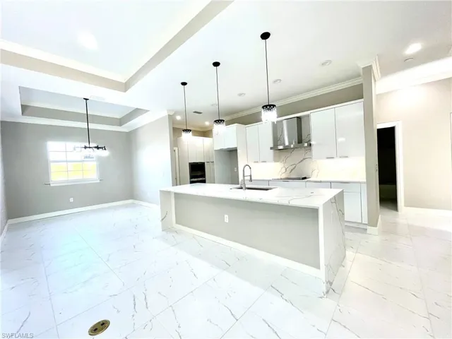 Kitchen featuring modern cabinets, light stone countertops, crown molding, hanging light fixtures, and white cabinets