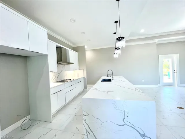 Kitchen featuring modern cabinets, white cabinets, light marble finish flooring, light stone counters, and wall chimney exhaust hood