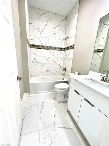 Bathroom with vanity, light marble finish floors, and bathing tub / shower combination