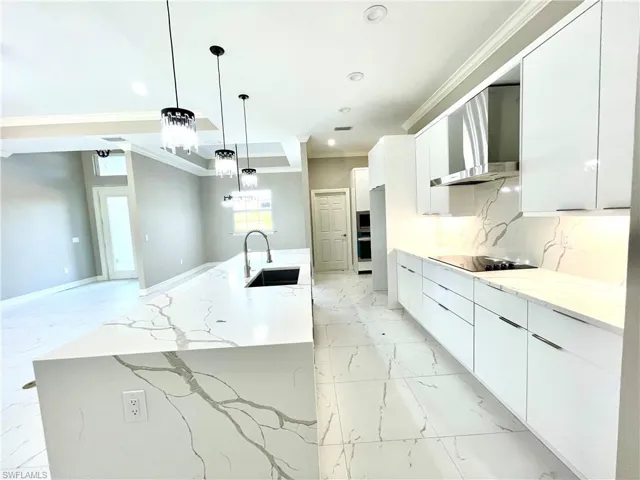 Kitchen featuring wall chimney range hood, ornamental molding, white cabinetry, light marble finish floors, and modern cabinets