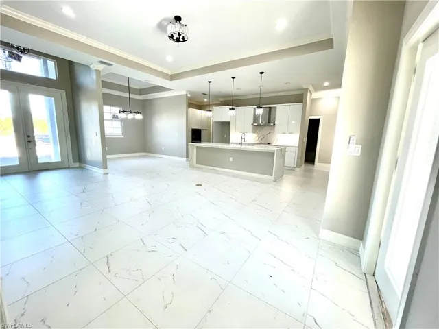 Unfurnished living room featuring crown molding, french doors, a raised ceiling, light marble finish floors, and recessed lighting