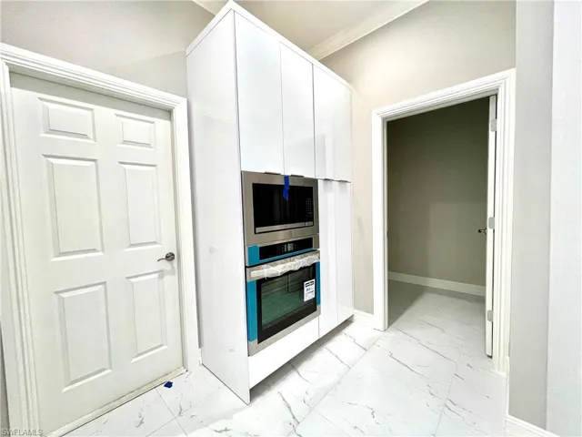 Kitchen with light marble finish flooring, crown molding, stainless steel appliances, and white cabinets