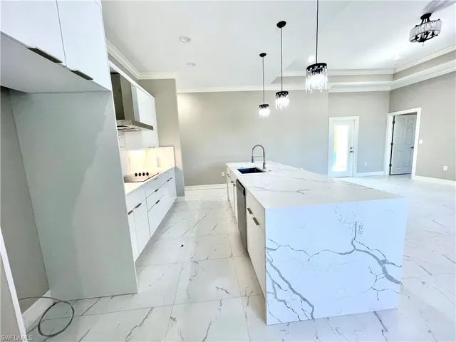 Kitchen with white cabinetry, modern cabinets, wall chimney exhaust hood, ornamental molding, and hanging light fixtures