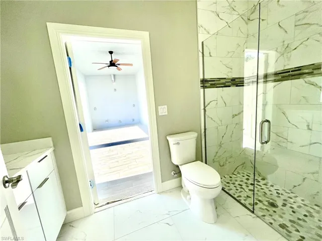Full bathroom with light marble finish floors, a marble finish shower, vanity, and a ceiling fan