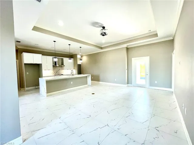 Unfurnished living room with crown molding, a raised ceiling, recessed lighting, and light marble finish flooring