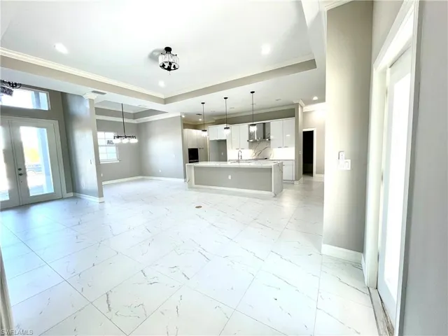 Unfurnished living room with crown molding, light marble finish flooring, french doors, a raised ceiling, and a chandelier