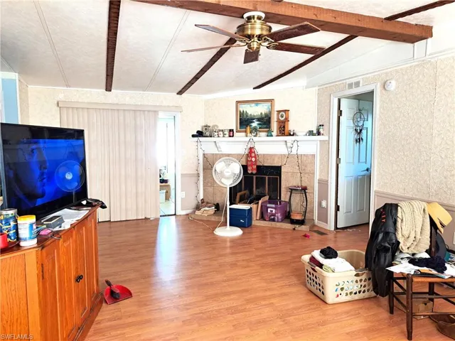 Living room featuring beam ceiling, a fireplace, ceiling fan, and light wood-type flooring