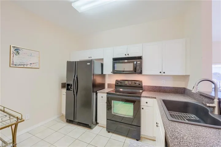 Kitchen featuring black appliances, white cabinets, light tile patterned floors, and sink