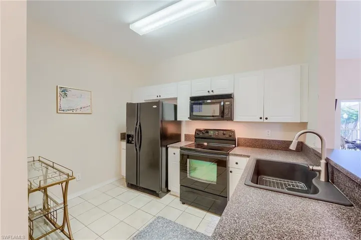 Kitchen featuring light tile patterned flooring, sink, white cabinets, and black appliances