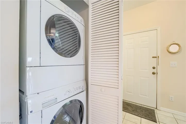 Clothes washing area with stacked washing maching and dryer and light tile patterned floors