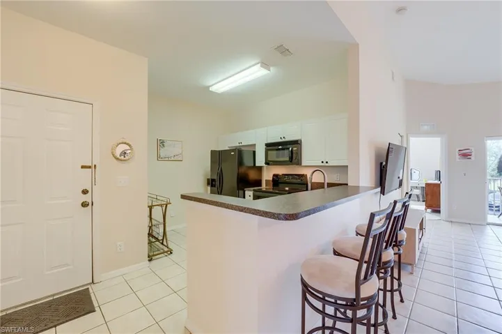 Kitchen with kitchen peninsula, a kitchen breakfast bar, black appliances, light tile patterned floors, and white cabinets