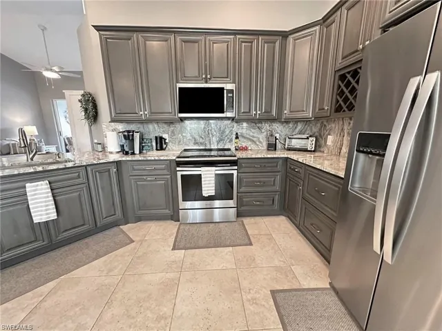 Kitchen featuring backsplash, ceiling fan, light stone countertops, light tile patterned flooring, and stainless steel appliances