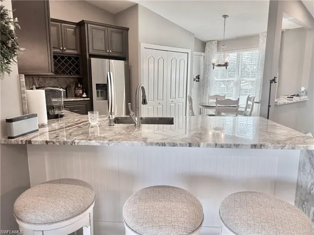 Kitchen featuring sink, stainless steel fridge with ice dispenser, a notable chandelier, lofted ceiling, and dark brown cabinets