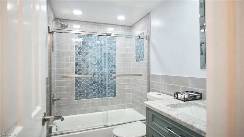 Full bathroom with tile walls, combined bath / shower with glass door, vanity, and toilet