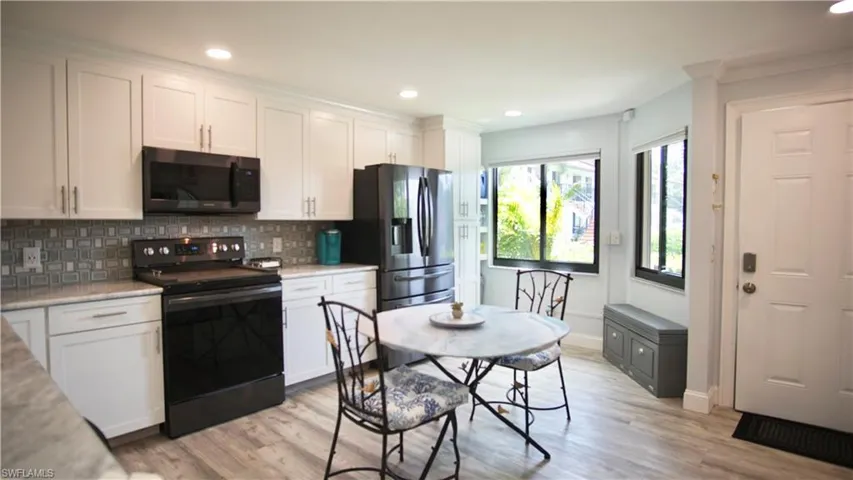Kitchen with light hardwood / wood-style floors, electric range oven, tasteful backsplash, and white cabinetry