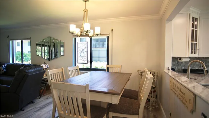 Dining area with a wealth of natural light, wood-type flooring, ornamental molding, and an inviting chandelier