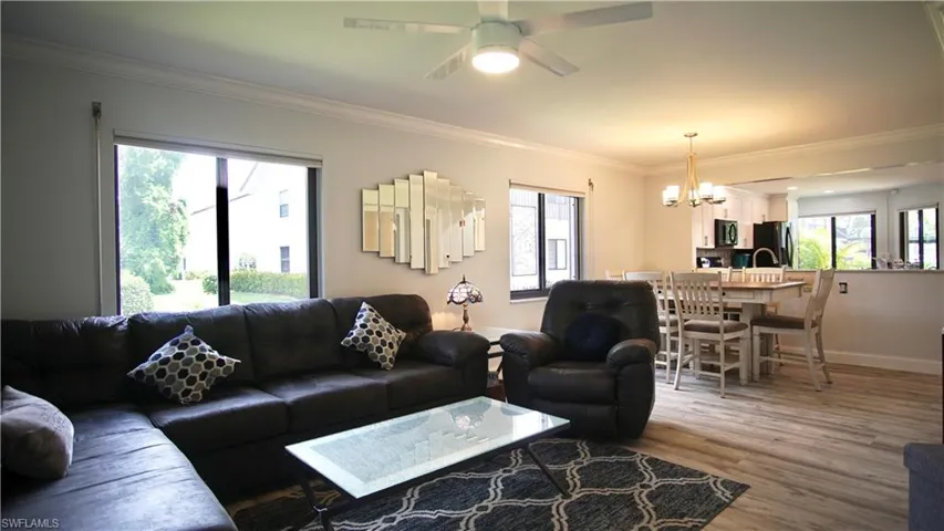 Living room featuring hardwood / wood-style flooring, ceiling fan with notable chandelier, and crown molding