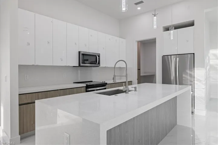 Kitchen with hanging light fixtures, white cabinetry, an island with sink, and stainless steel appliances