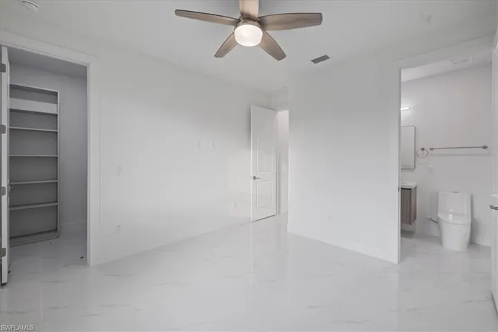 Unfurnished bedroom featuring ensuite bathroom, a spacious closet, ceiling fan, and a closet