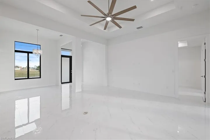 Empty room with ceiling fan with notable chandelier and a raised ceiling