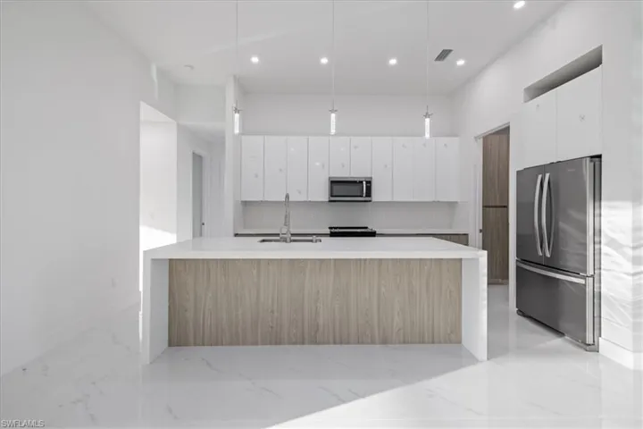 Kitchen featuring pendant lighting, sink, white cabinetry, stainless steel appliances, and an island with sink