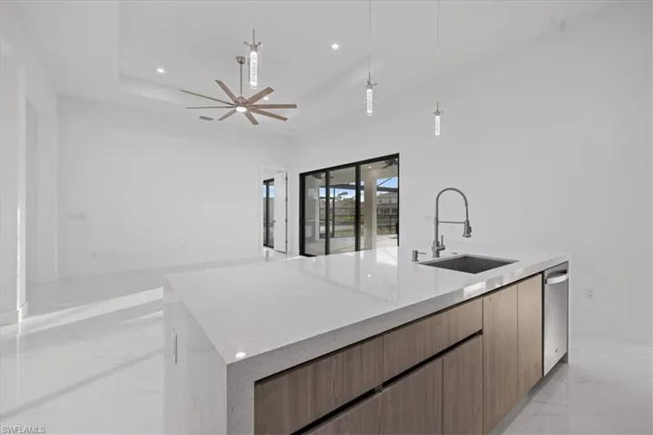 Kitchen featuring sink, light stone counters, hanging light fixtures, a raised ceiling, and a kitchen island with sink