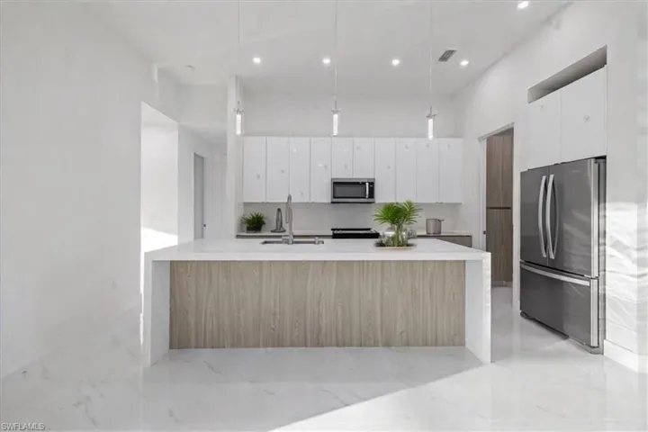Kitchen with appliances with stainless steel finishes, pendant lighting, sink, white cabinets, and a center island with sink