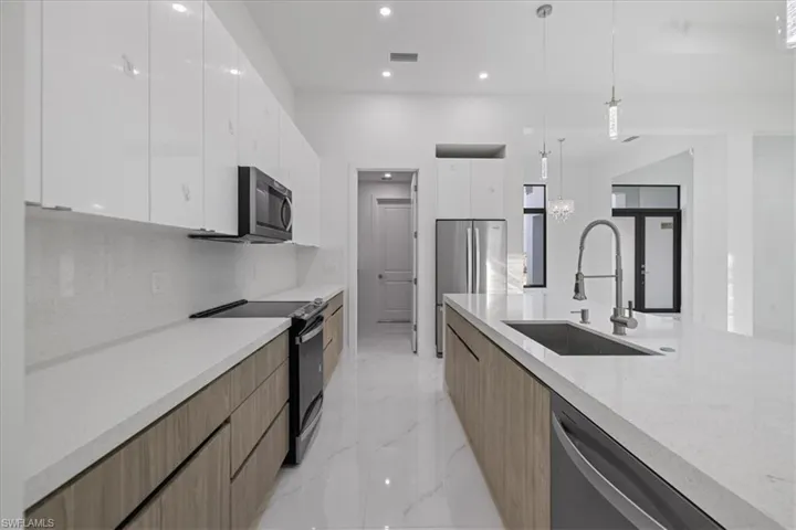 Kitchen with white cabinetry, sink, backsplash, hanging light fixtures, and stainless steel appliances