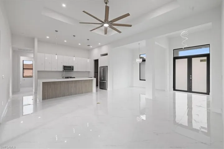Kitchen with a raised ceiling, white cabinetry, hanging light fixtures, stainless steel appliances, and a spacious island