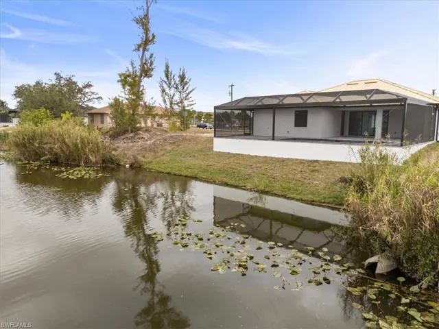 Back of property with a water view, a patio, a lanai, and a yard