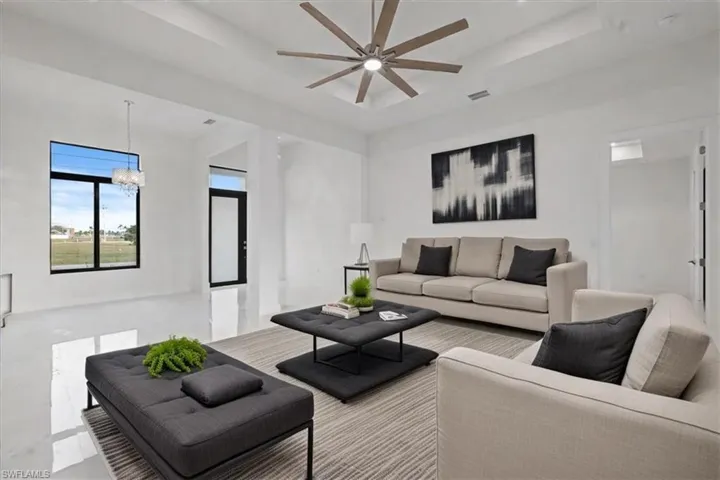 Living room featuring a tray ceiling and ceiling fan with notable chandelier