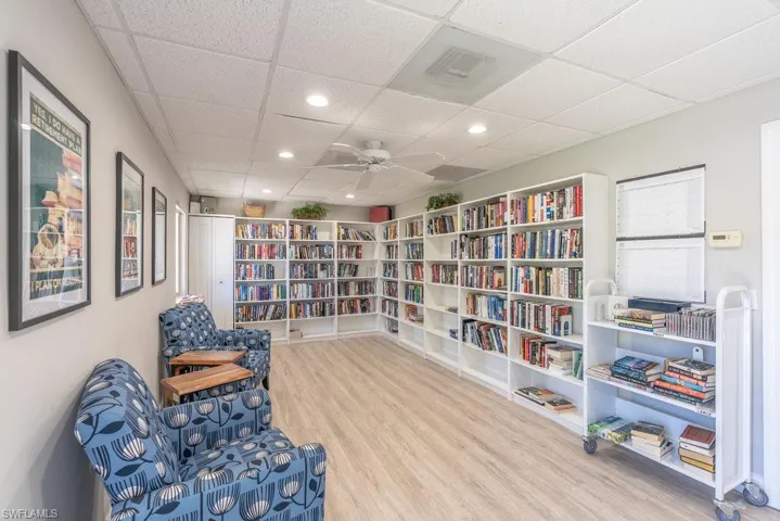 Living area featuring a paneled ceiling, bookshelves, recessed lighting, wood finished floors, and ceiling fan
