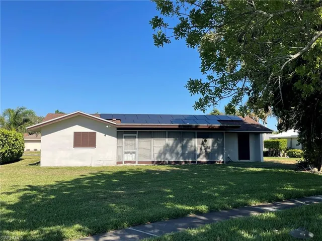 Back of house featuring solar panels, a lawn, and stucco siding