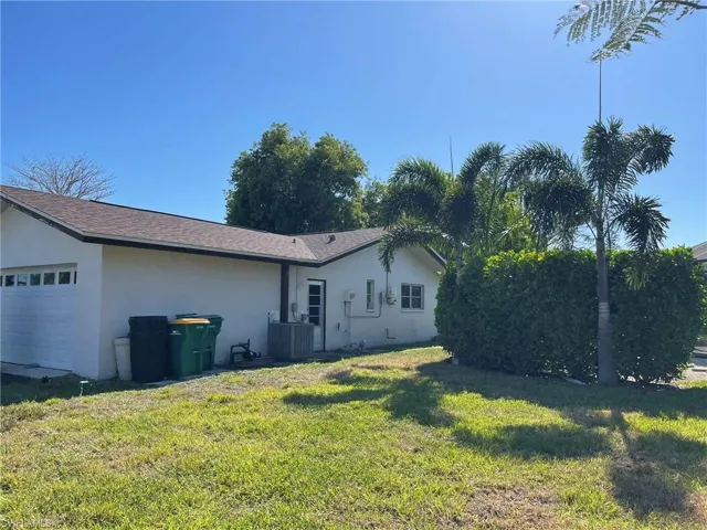 Side of property with an attached garage, stucco siding, a lawn, and roof with shingles