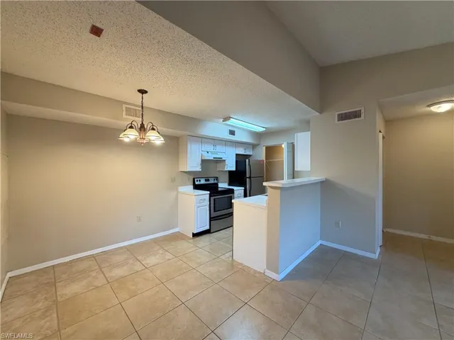 Kitchen featuring white cabinets, stainless steel range with electric stovetop, light countertops, a textured ceiling, and pendant lighting