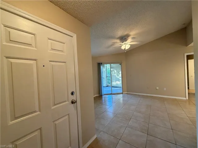 Unfurnished room with a textured ceiling, light tile patterned floors, a ceiling fan, and lofted ceiling