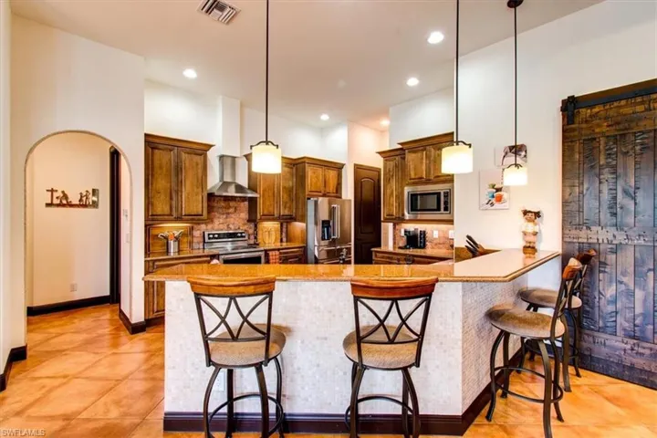 Kitchen featuring wall chimney range hood, decorative light fixtures, a kitchen bar, kitchen peninsula, and stainless steel appliances