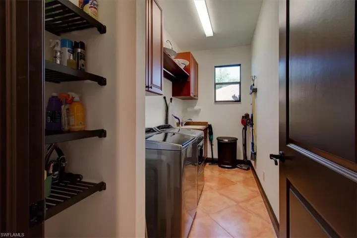 Clothes washing area with cabinets, light tile patterned floors, washing machine and dryer, and sink