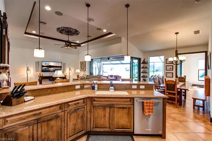 Kitchen with ceiling fan with notable chandelier, a tray ceiling, sink, light tile patterned floors, and decorative light fixtures