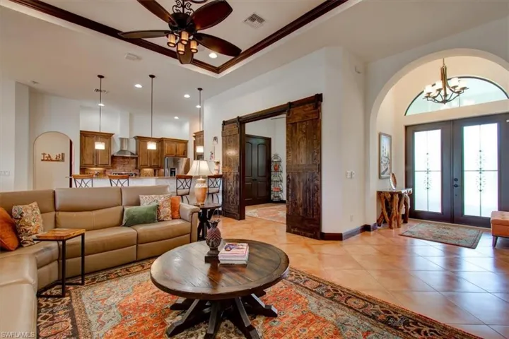 Living room with a towering ceiling, french doors, ceiling fan with notable chandelier, and crown molding