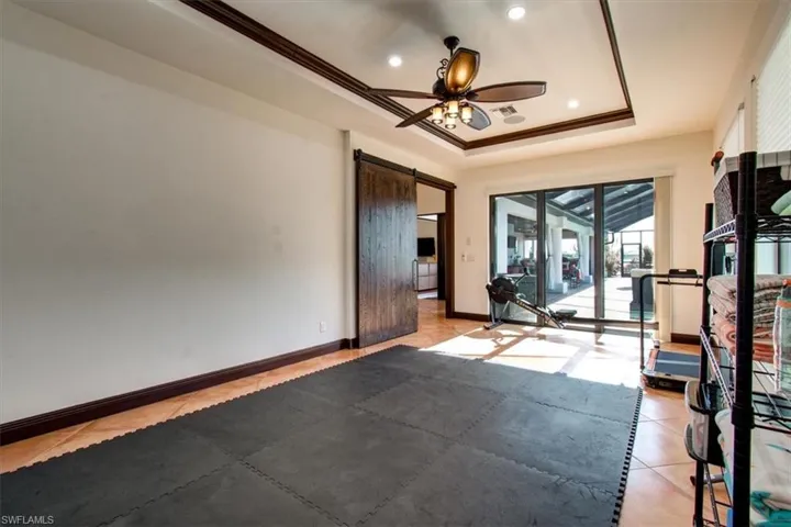 Workout room with a raised ceiling, a barn door, ceiling fan, and ornamental molding