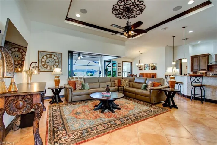 Living room featuring a raised ceiling, ceiling fan with notable chandelier, and ornamental molding