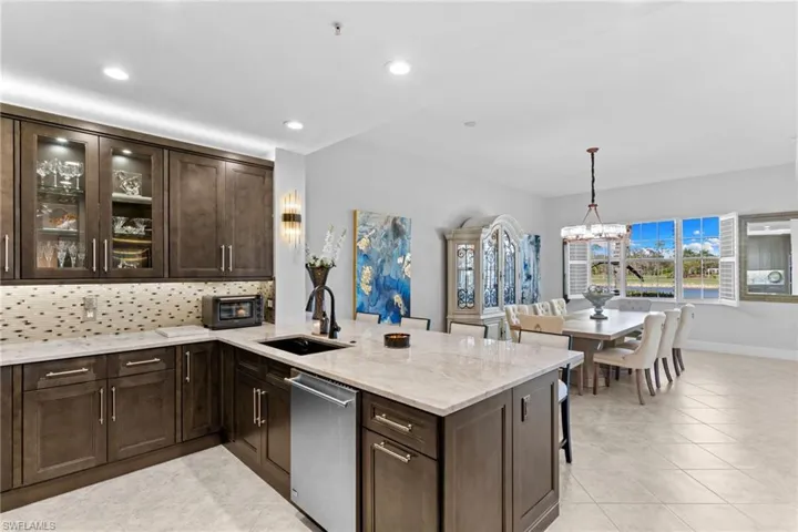 Kitchen with dark wood finish cabinetry, a peninsula, light stone countertops, backsplash, and glass fronted cabinets