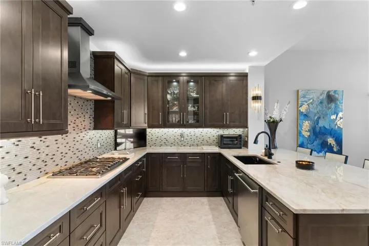Kitchen with a peninsula, dark wood finish cabinetry, glass fronted cabinets, light stone countertops, and a kitchen breakfast bar
